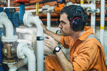 Marine engineer inspecting ship's engine with torchlight in engine control room ECR. Seamen's work.