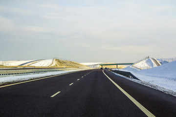 Canvas Print - Modern wide smooth empty asphalt highway stretching to horizon under high bridge turning right past distant forest at day. Speed, comfortable journey and professional road building concept.