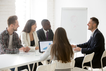 Smiling ceo talking to multiracial team at office meeting, friendly executive discussing good news laughing at group briefing negotiations, coach mentor joking speaking to business people at training