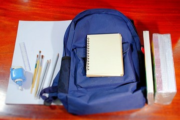 Blue student bag with pencil brush, pencil sharpener and blank book On a wooden background