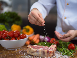 Chef putting salt on juicy slice of raw steak