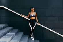 Woman In Sportswear Relaxing After Workout, Standing On Staircase