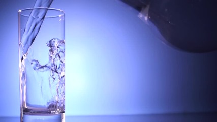 Wall Mural - Pouring Water into Glass from a jug, on blue background.