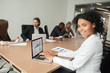 © fizkes - Smiling millennial african businesswoman looking at camera at meeting, female afro american marketing manager using laptop at group office briefing, young black project sales professional portrait