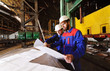 © Evgeniy Kalinovskiy - Two workers in construction helmets discuss a plan, blueprint or industrial project in the background of the plant