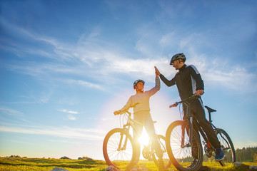 happy couple goes on a mountain road in the woods on bikes with helmets giving each other a high five