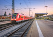 High speed red train on the railway station at sunset. Nuremberg, Germany. Colorful urban landscape. Modern intercity train on the railway platform at night. Commuter passenger train on railroad. Dusk