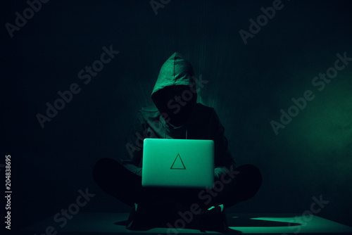 Fotografía toned picture of silhouette of hacker in hoodie using laptop