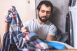 © LIGHTFIELD STUDIOS - handsome loner taking clothes for washing near washing machine in bathroom