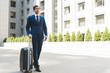 © LIGHTFIELD STUDIOS - attractive young businessman in stylish suit with luggage walking by business district