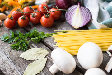 Fresh ingredients for cooking pasta, tomato and spices over wooden table background with copy space