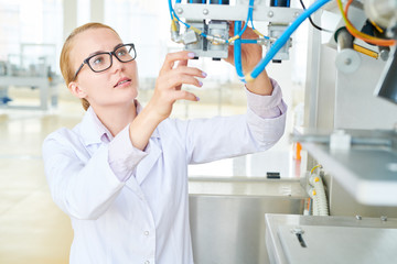 Wall Mural - Waist-up portrait of hard-working technician wearing white coat adjusting equipment of modern dairy factory, interior of spacious production department on background