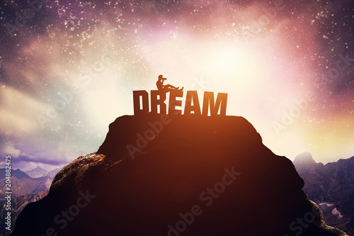 Photographie Boy sitting on a DREAM writing on the peak of a mountain.