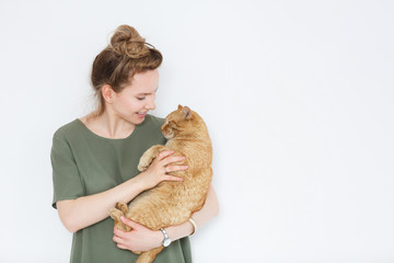 portrait handsome young hipster woman, hugs his good friend ginger cat on white wall background. Positive human emotions, facial expression, feelings. People and animals in love