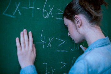 Wall Mural - Teenager girl in math class overwhelmed by the math formula. Pressure, Education, Success concept. Student with head against blackboard.