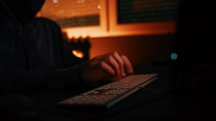 Computer hacker typing keyboard in dark interior, low key footage