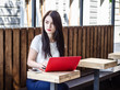 © Todayphoto - Beautiful brunette girl sitting on bench at table in street cafe with  red laptop looking away