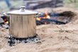 stainless steel pot being used to cook a camping meal with coals and a wood burning camp fire