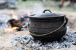 cast iron pot being used to cook a camping meal with coals and a wood burning camp fire