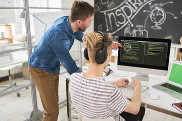 Wall Mural - Back view portrait of two contemporary young men in casual wear coding using computer collaborating  on startup project in modern office, copy space