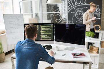 Back view portrait of contemporary program developer writing code sitting at desk with computer and working on startup project in modern office, copy space