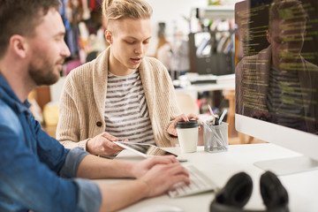 Wall Mural - Portrait of creative young man writing code sitting at desk using computer and collaborating with colleague on startup project in modern office