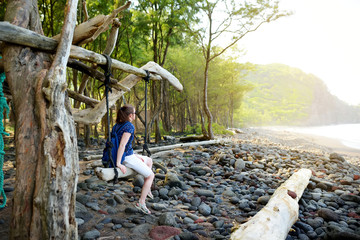 Poster - Young female tourist relaxing on a handmade swing on rocky beach of Pololu Valley on Big Island of Hawaii