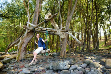 Poster - Young female tourist relaxing on a handmade swing on rocky beach of Pololu Valley on Big Island of Hawaii