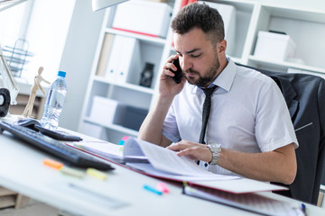 Wall Mural - A man is sitting in the office, working with documents and talking on the phone.