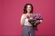 © oes - A young slender girl in stylish clothes is holding a bouquet of purple flowers. She is surprised at the gift she was given on a date. On a pink background with space for text