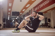 © HD92 - one young man, ordinary average man, exercise abs, sideways, sitting on floor, in gym. Unrecognizable people behind (out of focus).