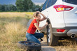 © Kyrylo Ryzhov - Young woman struggling to change flat car tire on countryside road