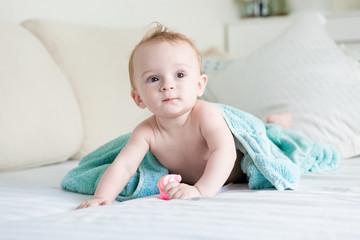 Wall Mural - Adorable 9 months old baby boy covered in blue towel crawling on bed