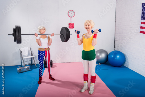 Fotografía smiling senior sportswomen exercising with dumbbells and barbell in gym
