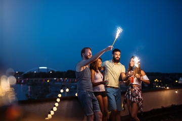 Wall Mural - Friends enjoying a rooftop party and dancing with sparklers