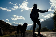 Young Girl On The Road Against The Background Of The Mountains With A Dog (hitch-hiking)