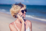 Fototapeta  - Young happy woman talking on mobile phone on a beach with sea background