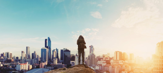 Wall Mural - a man with backpack standing on the mountain enjoying beautiful sunrise in the city