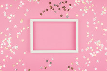 White Picture Frame And Sequins Stars On Pink Background. Top View, Flat Lay. Mockup For Party Or Birthday Invitation.