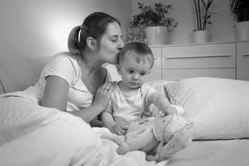 Wall Mural - Black and white portrait of young mother kissing her baby son before going to sleep