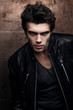© Bakulov - Handsome young man in stylish black leather jacket. Fashion model in dark clothes against the wall.