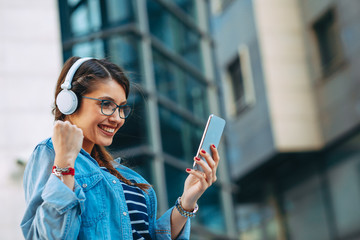 Wall Mural - Young woman making video call via smartphone and headphones  in the city