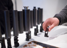 Flash Suppressors Or Muzzle Brakes Of A Modern Assault Rifles. Silencers, Sound Suppressors, Or Sound Moderators For Differently Calibrated Modern Weapons. The Man's Hand Holds The Device In His Hand.