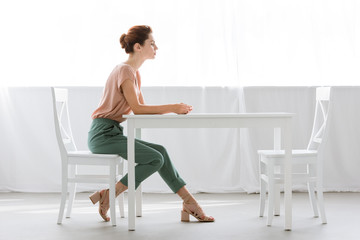 side view of attractive young woman sitting at table alone at home