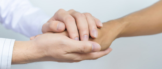 Two people holding hands for comfort. Doctor consoling relatives of patients in hospital concept banner panoramic crop for copy space.