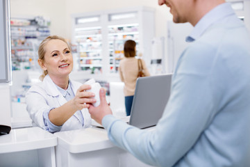 Wall Mural - Try this. Attractive female pharmacist assisting man and looking at him