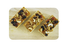 Three Pieces Of Fruitcake Topped With Mix Fruits And Cashew Nuts On Wooden Cutting Board Isolated On White Backgrond With Clipping Path