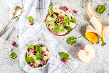 Wall Mural - Healthy summer breakfast, fruit and berry salad with spinach, granola, apple and banana, white marble background  above