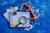 Fototapeta Dmuchawce - Travel flat lay with wooden anchor, fantasy map, watercolor sketches, seashells and compass on a navy blue background with copy space. Creative artist workplace in shades of blue