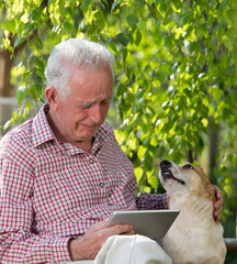 Wall Mural - Old man with dog and tablet crying in garden